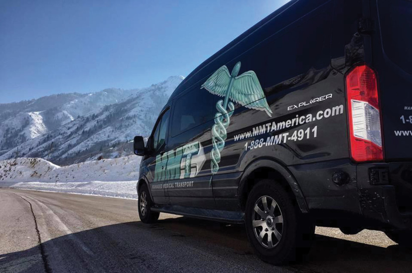 A medical transport van parked on a snowy road with mountains in the background.